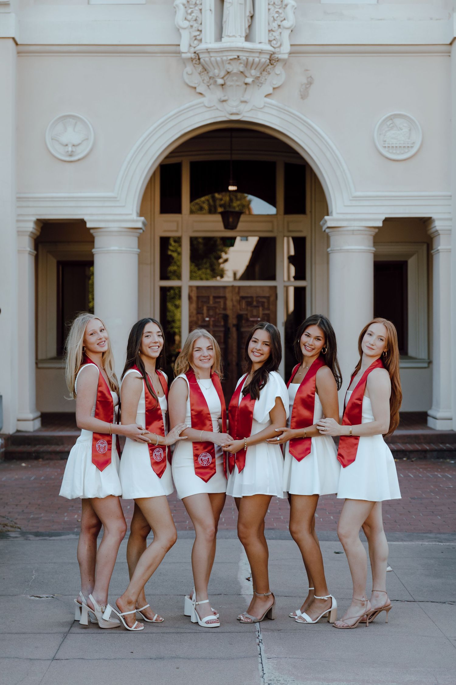 Group of Santa Clara University graduates pose for photoshoot in front of architecture. Taken by Bay Area Graduation Photographer.