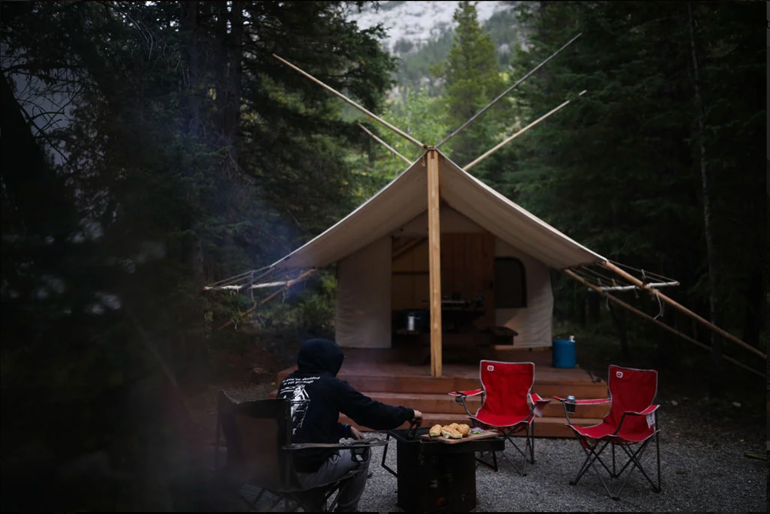 a glamping tent in the forest with chairs out front around a firepit