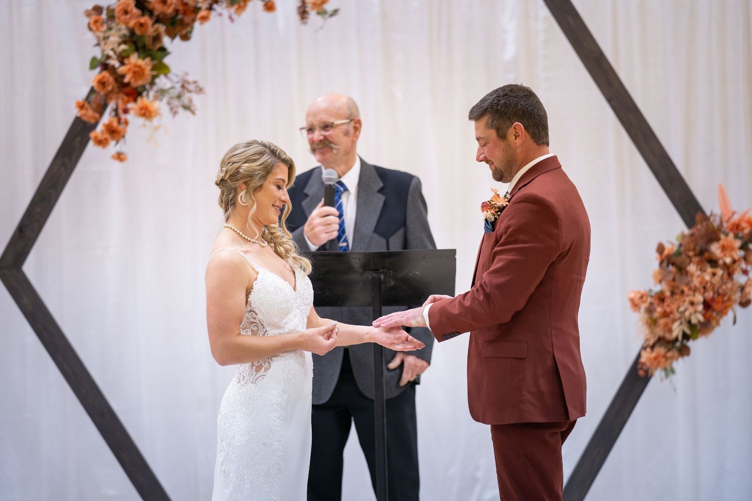 A wedding ceremony takes place in front of white curtains decorated with orange autumn leaves and branches.