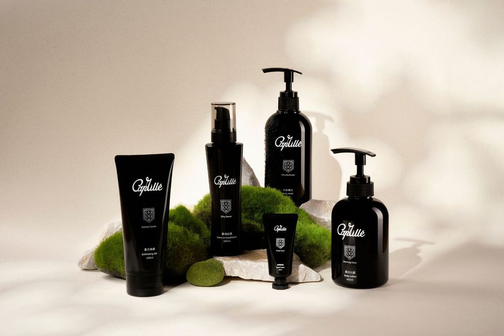 Black luxury skincare and haircare products arranged on white surface with green leaves as decorative elements.