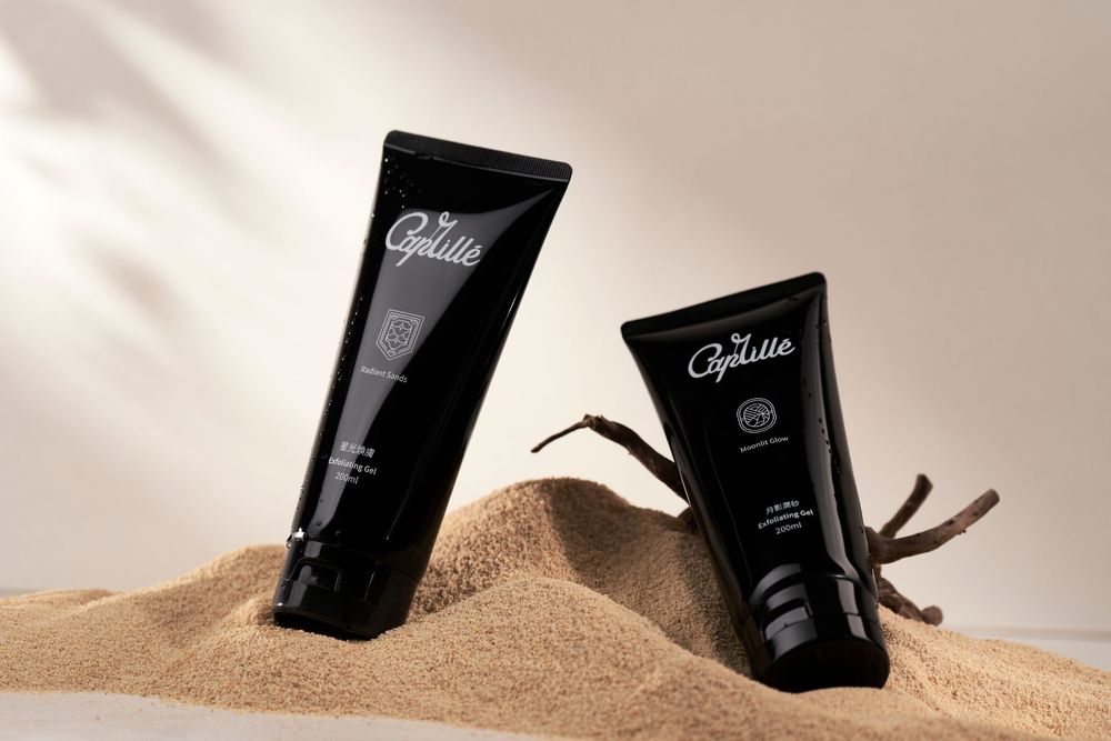 Two black skincare tubes arranged on beige sand with soft shadows and minimal styling.
