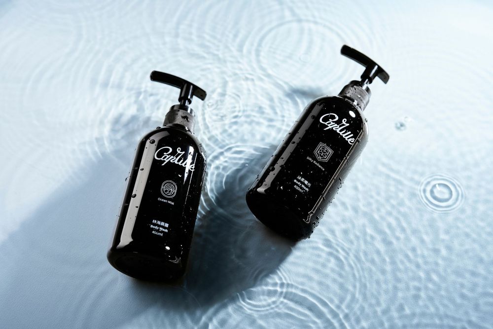 Two black pump bottles of personal care products reflecting on a wet surface with rippling water effects.