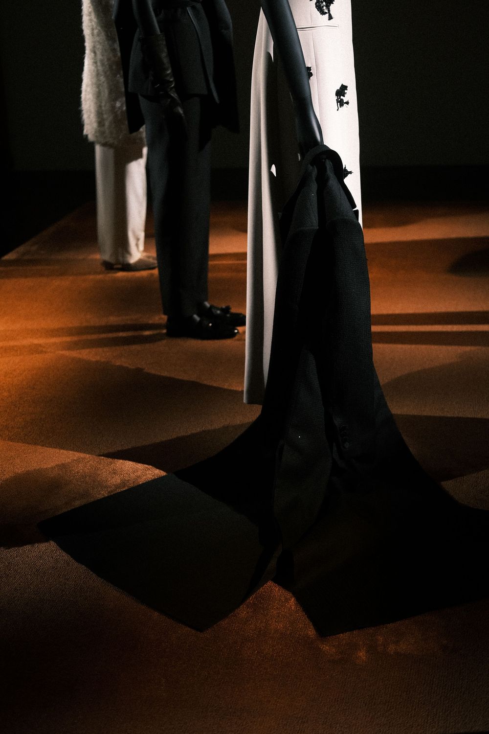 Dramatic low-angle view of dark silhouettes against warm lighting on a stage floor during a fashion show.