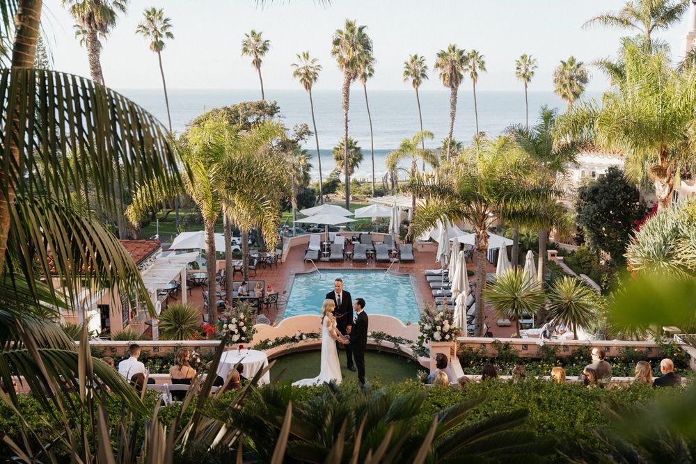 A scenic wedding ceremony overlooking a resort pool with palm trees and ocean views in the background.