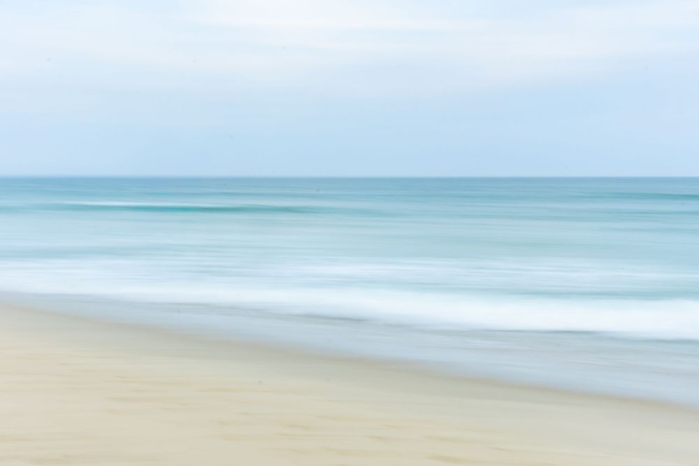 Soft focus beach landscape with gentle waves rolling onto sandy shore against pale turquoise ocean and hazy sky on Nantucket, MA