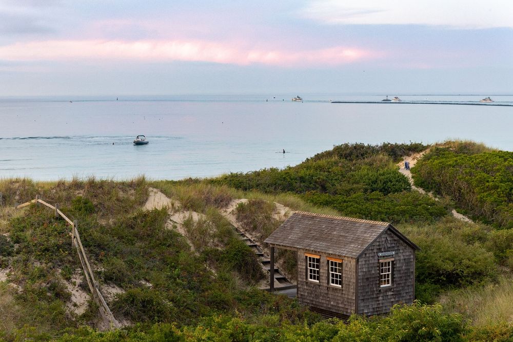A scenic coastal landscape featuring beach cottage Le Shack nestled among sand dunes at sunset on Steps Beach on Nantucket, MA.