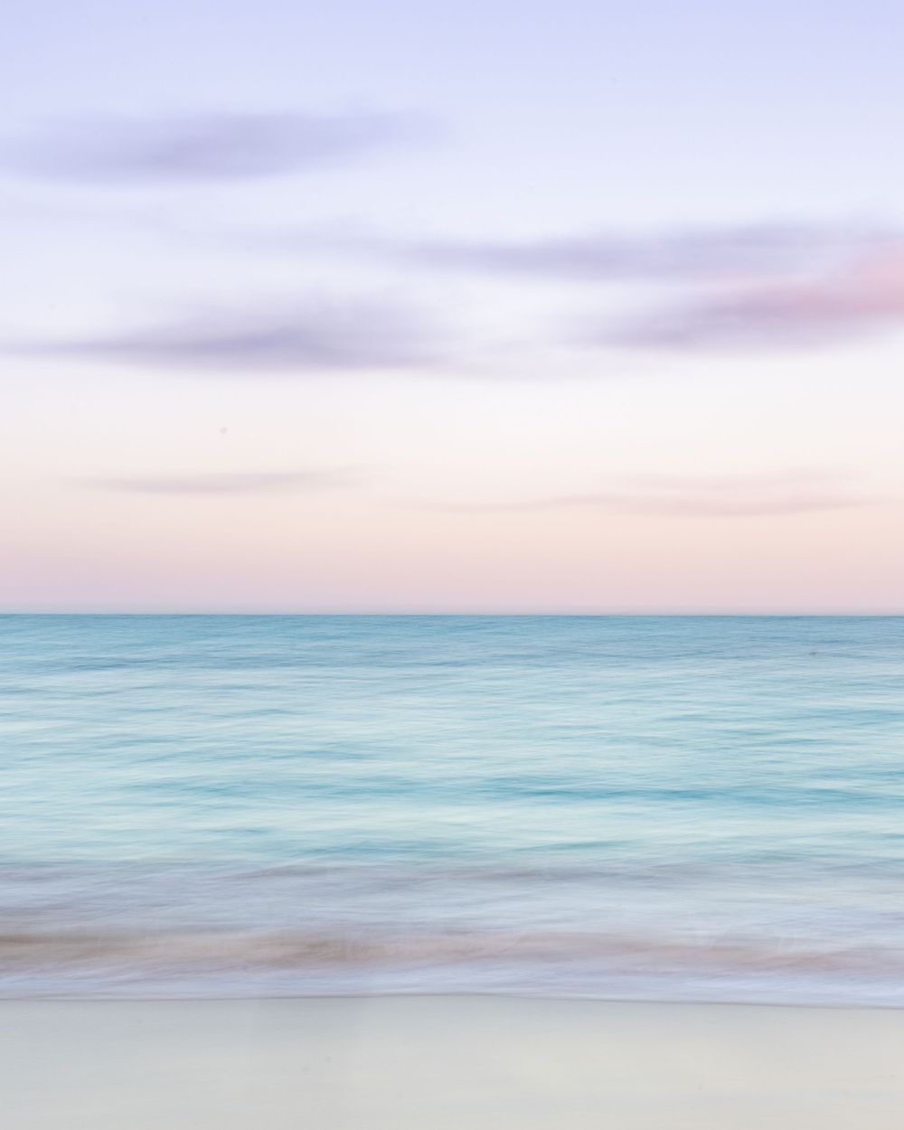 Dreamy long exposure seascape with soft pastel colors of turquoise water and pink sky over smooth sandy beach at Dawn Beach St. Maarten.