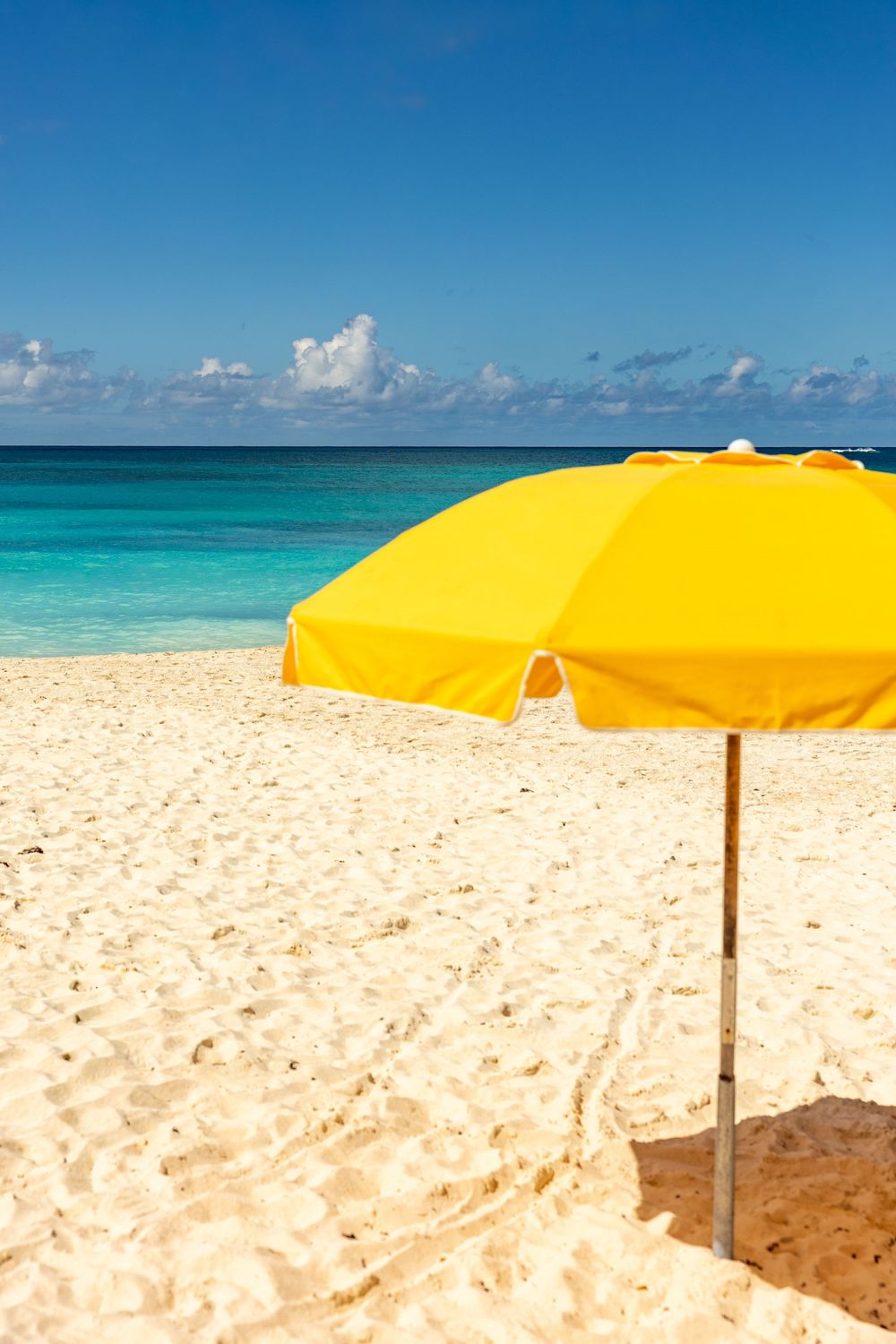 Bright yellow beach umbrellas line a pristine white sand beach against turquoise waters & blue sky in the Caribbean Shoal Beach Anguilla