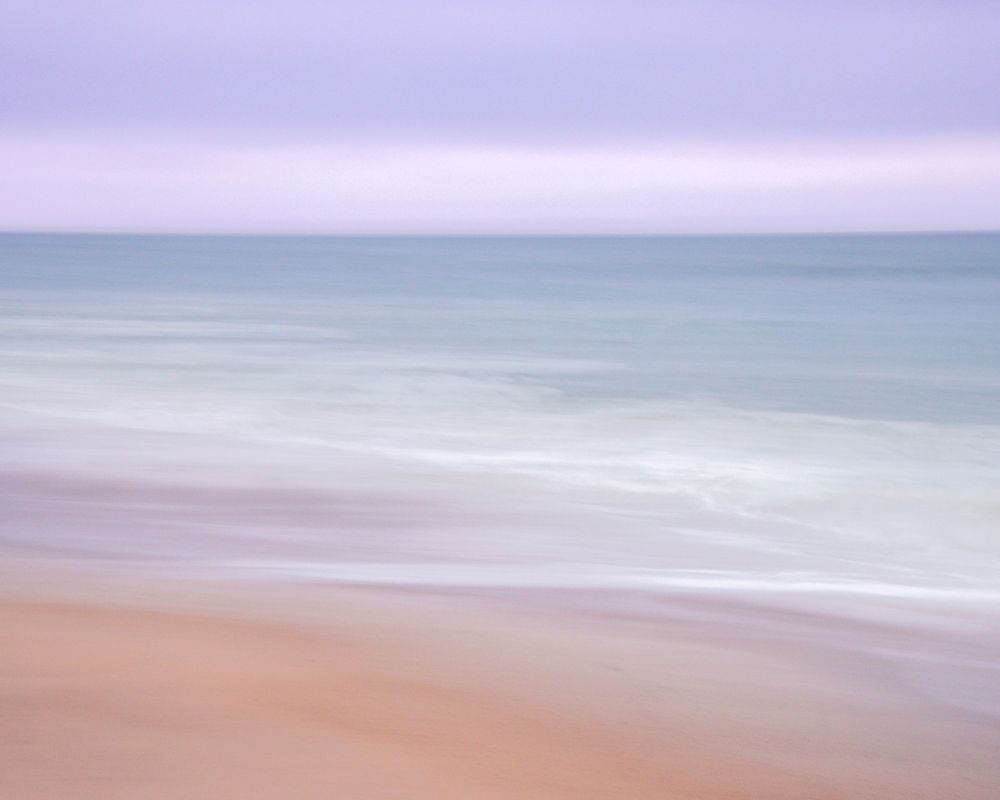 A tranquil beach scene with soft pastel colors shows waves gently rolling onto the sandy shore during sunset in Madaket- Nantucket, MA.