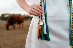 Couple in western wedding attire holds hands while horses graze in the desert background at sunset.