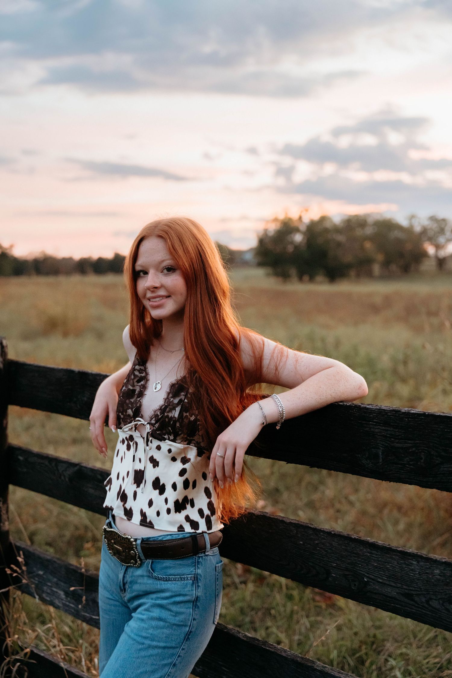 A polka dot top and jeans outfit photographed against a rustic wooden fence at golden hour in a pastoral field setting.