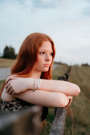 Artistic portrait showing someone resting their arms on a fence during sunset with soft lighting and bokeh effects.
