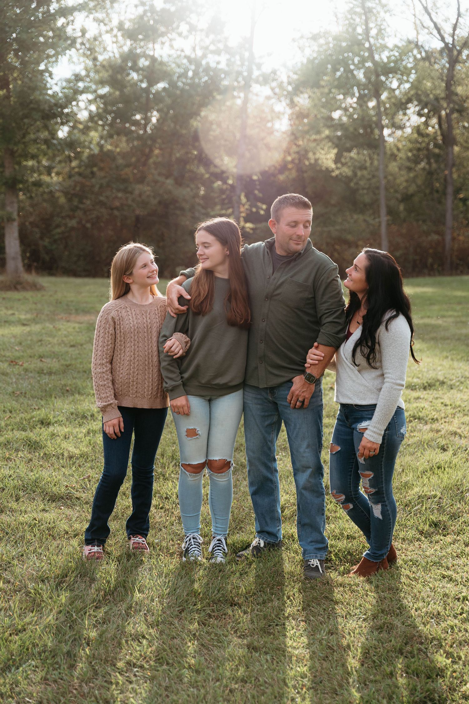 A group of people laughing together while standing in a sunlit grassy field during golden hour.