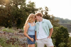 Young couple sharing a romantic moment outdoors at golden hour with lush green trees in the background.