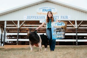 A black and white pig stands with its handler in front of the Jefferson County Fair exhibition building.