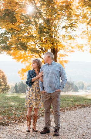 A couple walks together on an autumn path with golden trees and sunlight filtering through the branches above.