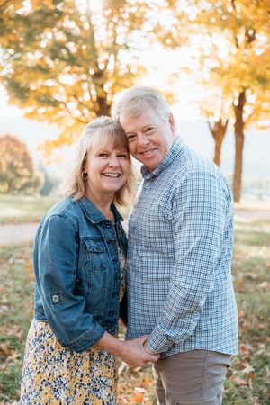 A couple shares a tender moment outdoors during autumn with golden sunlit trees in the background.