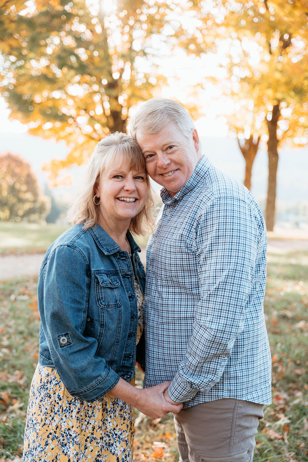 A couple shares a tender moment outdoors during autumn with golden sunlit trees in the background.