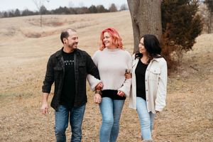 Three friends walking together and laughing in a field during autumn with brown grass and trees in the background.