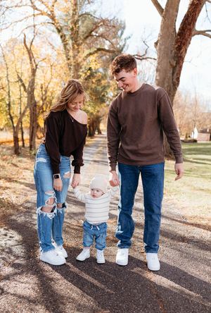 Family walking together on an autumn path through a park with fallen leaves and bare trees in the background.