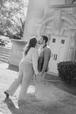 A romantic black and white portrait of a couple sharing an intimate moment outdoors near a classic architectural facade.