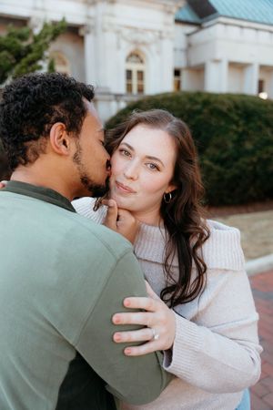 A couple in a cozy white sweater and olive jacket share intimate moments in a romantic outdoor photoshoot.