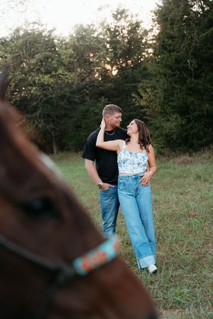 A couple in casual attire shares romantic moments together during a sunset photoshoot in a grassy field.