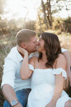 A romantic couple in white outfits share tender kisses during a golden hour outdoor photo session.