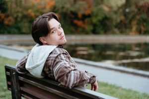A person relaxes on a wooden bench near a tranquil pond on an autumn day.