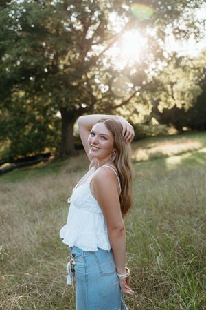 Woman in white top and jeans laughing joyfully in a sunlit field during golden hour.