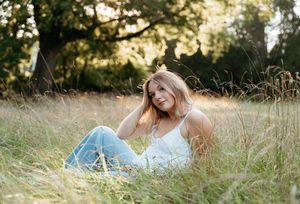 Person lying in tall grass field at golden hour with sunlight filtering through grass blades.