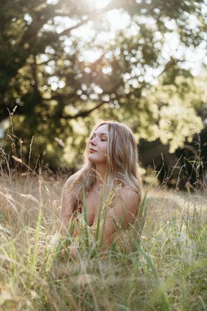 Person with long blonde hair lying in tall grass during golden hour sunlight.