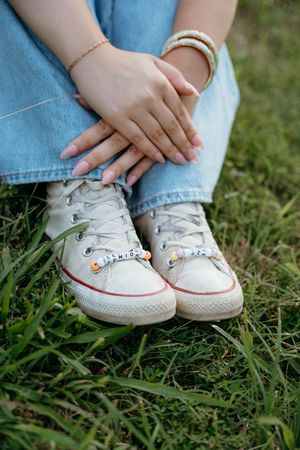 Close-up of small white Converse sneakers with decorative charms worn with blue jeans on grass.