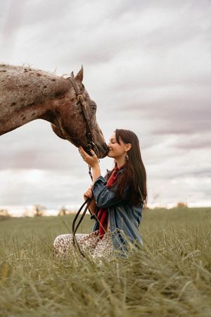 A young girl in denim shares a tender moment with a brown horse in a misty field at sunset.