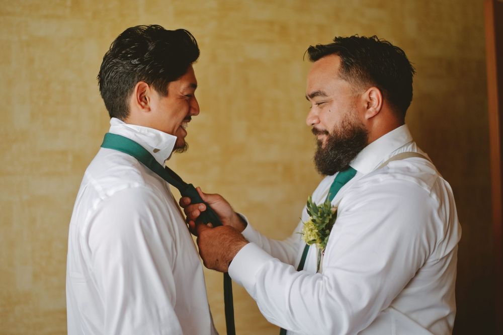 Two people in white dress shirts help each other adjust their matching turquoise bow ties before a formal event.
