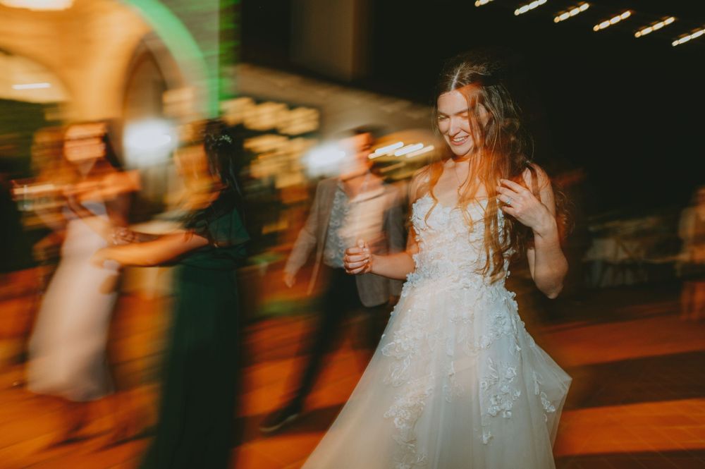 A bride in a flowing white gown spins and dances joyfully during a nighttime wedding celebration.