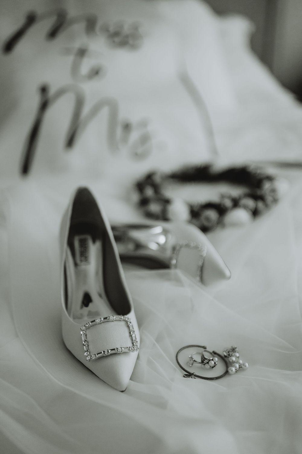 A series of elegant white wedding shoes arranged in a row on soft white fabric, photographed in black and white.