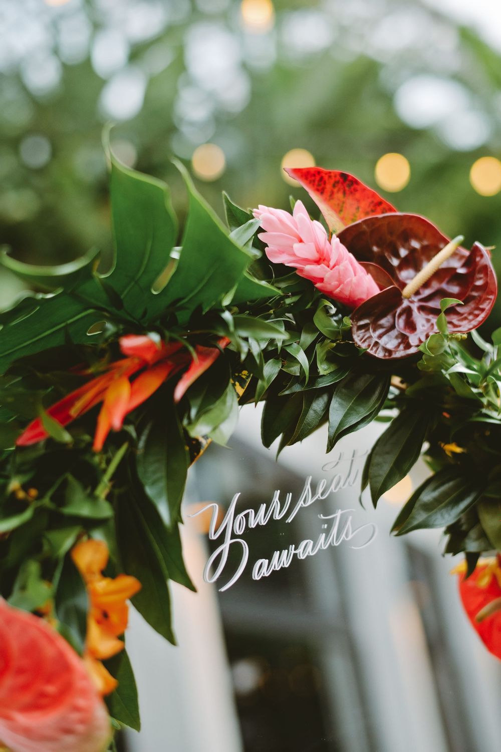 Wedding reception decor featuring a floral garland with red flowers and green leaves against a soft bokeh background.