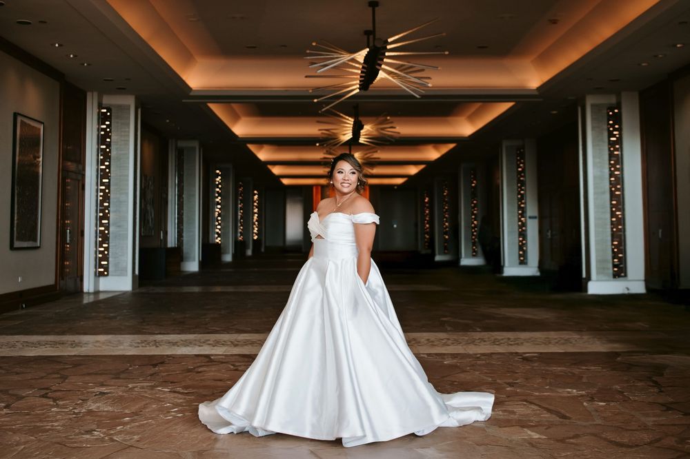 A bride in a flowing white strapless wedding gown walks through a dimly lit industrial hallway.