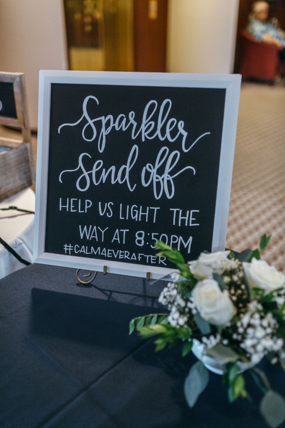 Wedding reception signage with chalkboard messages and white floral accents.