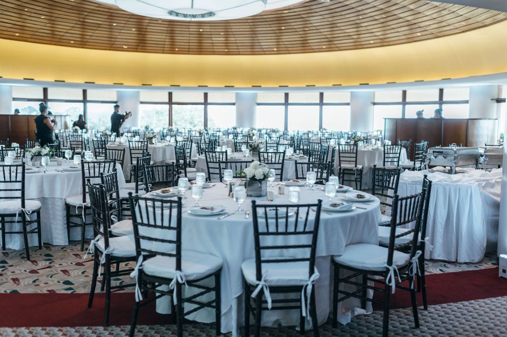 Spacious wedding reception venue with white tablecloths and black chiavari chairs.