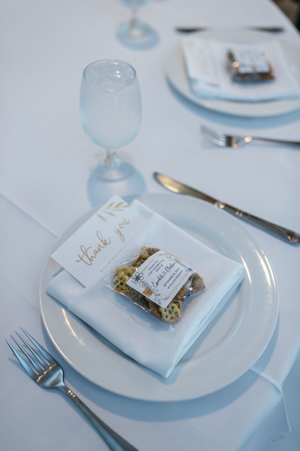 Elegant place settings with white plates and personalized favor bags.