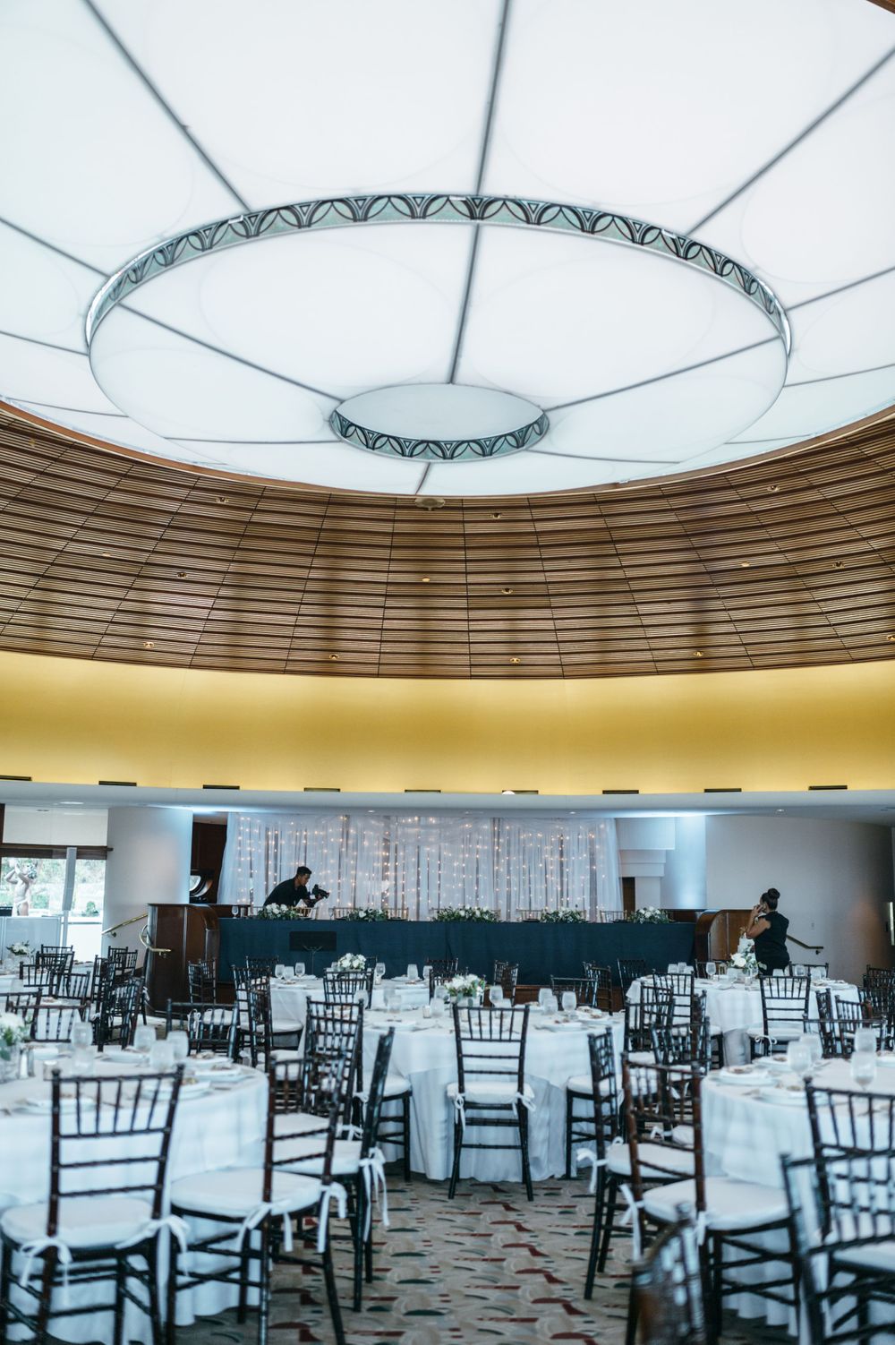 Modern wedding venue with geometric ceiling design and black chiavari chairs.