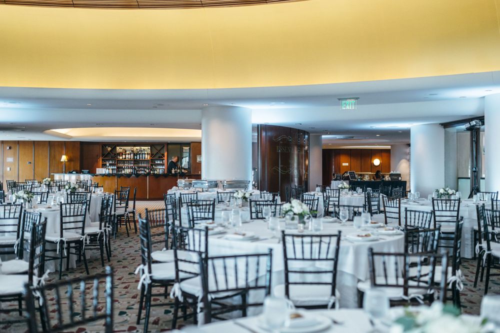 Elegant wedding reception hall setup with black chiavari chairs and white tablecloths.