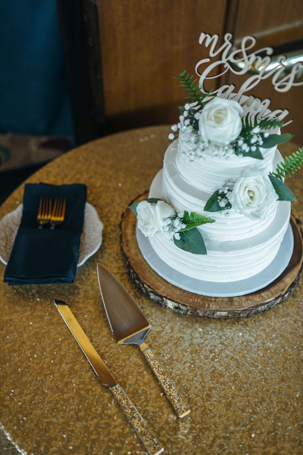 White wedding cake with fresh floral decorations on a textured gold surface.