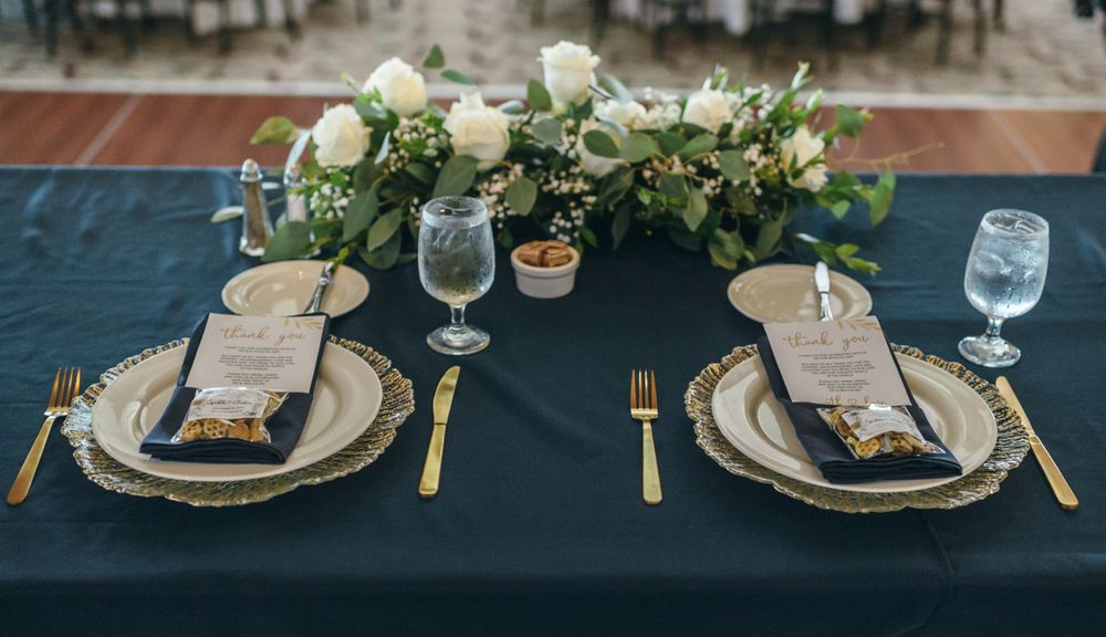Elegant navy and gold wedding table setting with floral centerpieces and place cards.