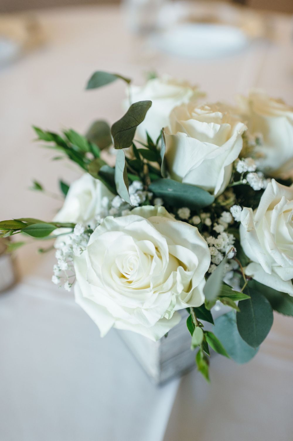 Elegant white roses and baby's breath floral arrangements with green eucalyptus leaves for wedding decor.
