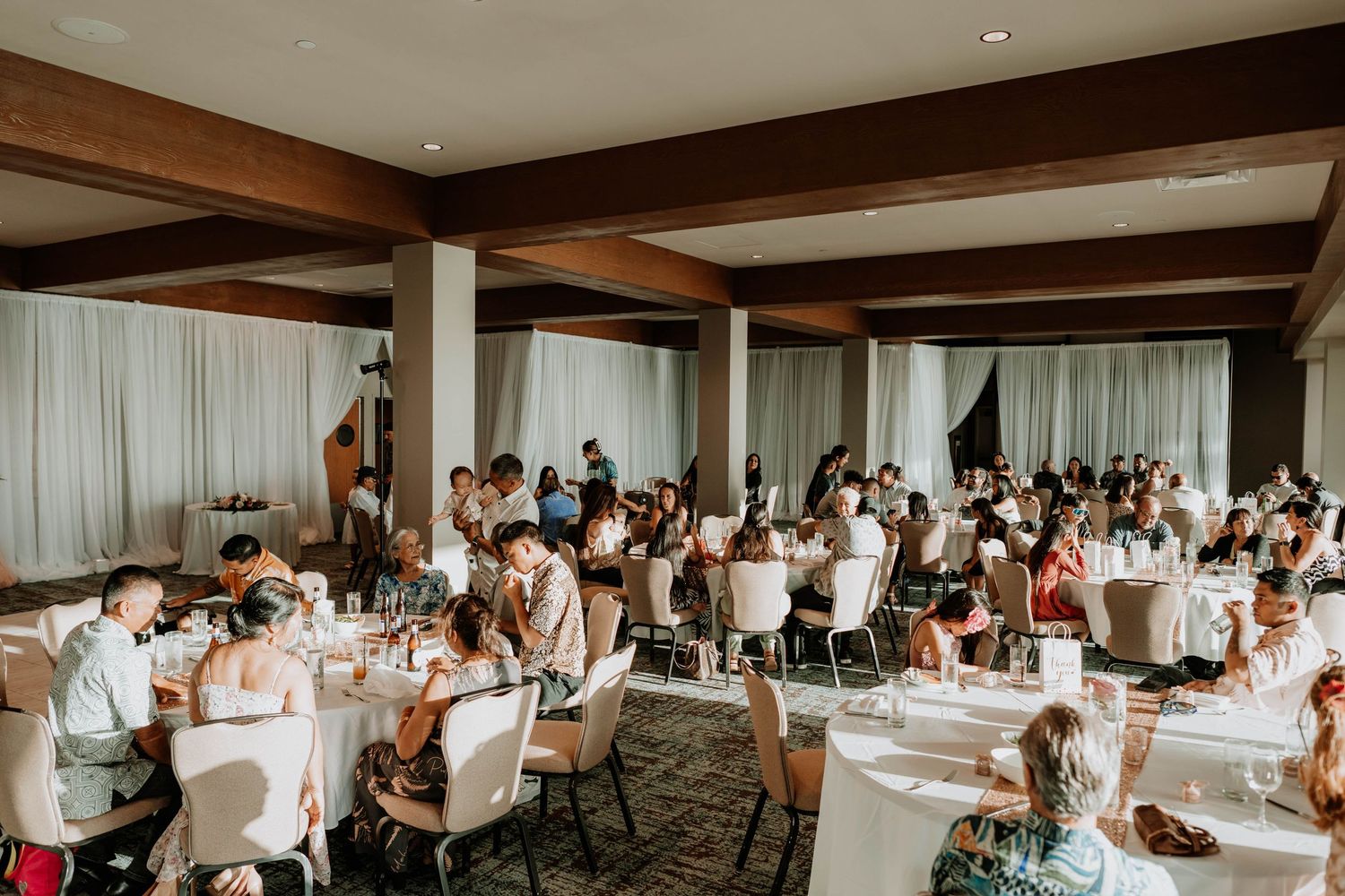 Spacious indoor wedding reception venue with white decor and wooden beam details.