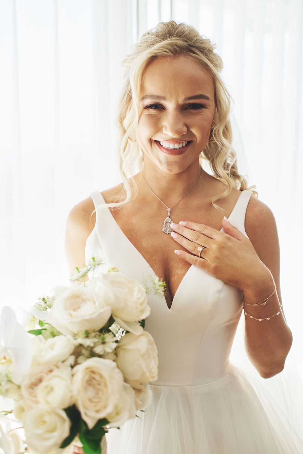 A bride in white holds a stunning bouquet of cream roses while laughing joyfully.