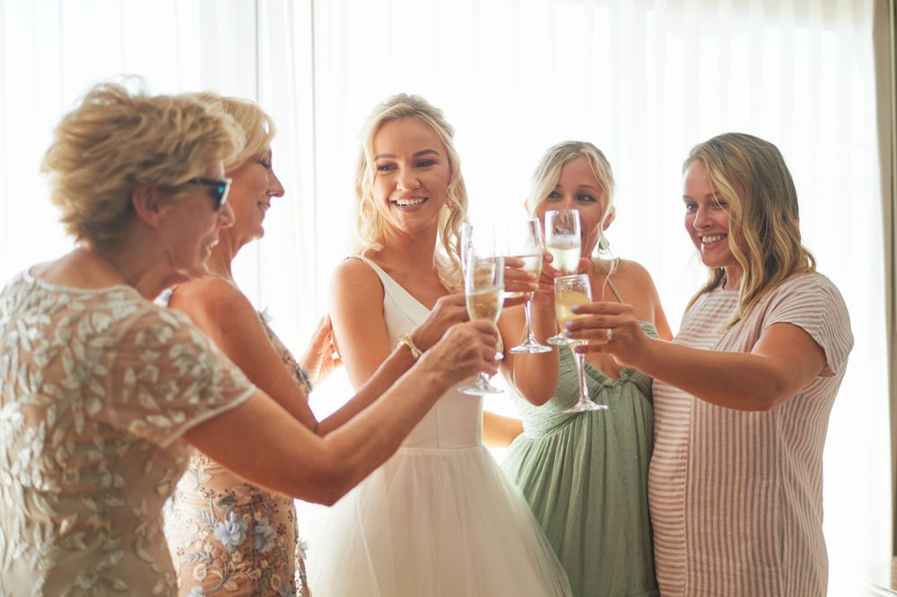 Wedding party members toast with champagne glasses during pre-ceremony preparations.